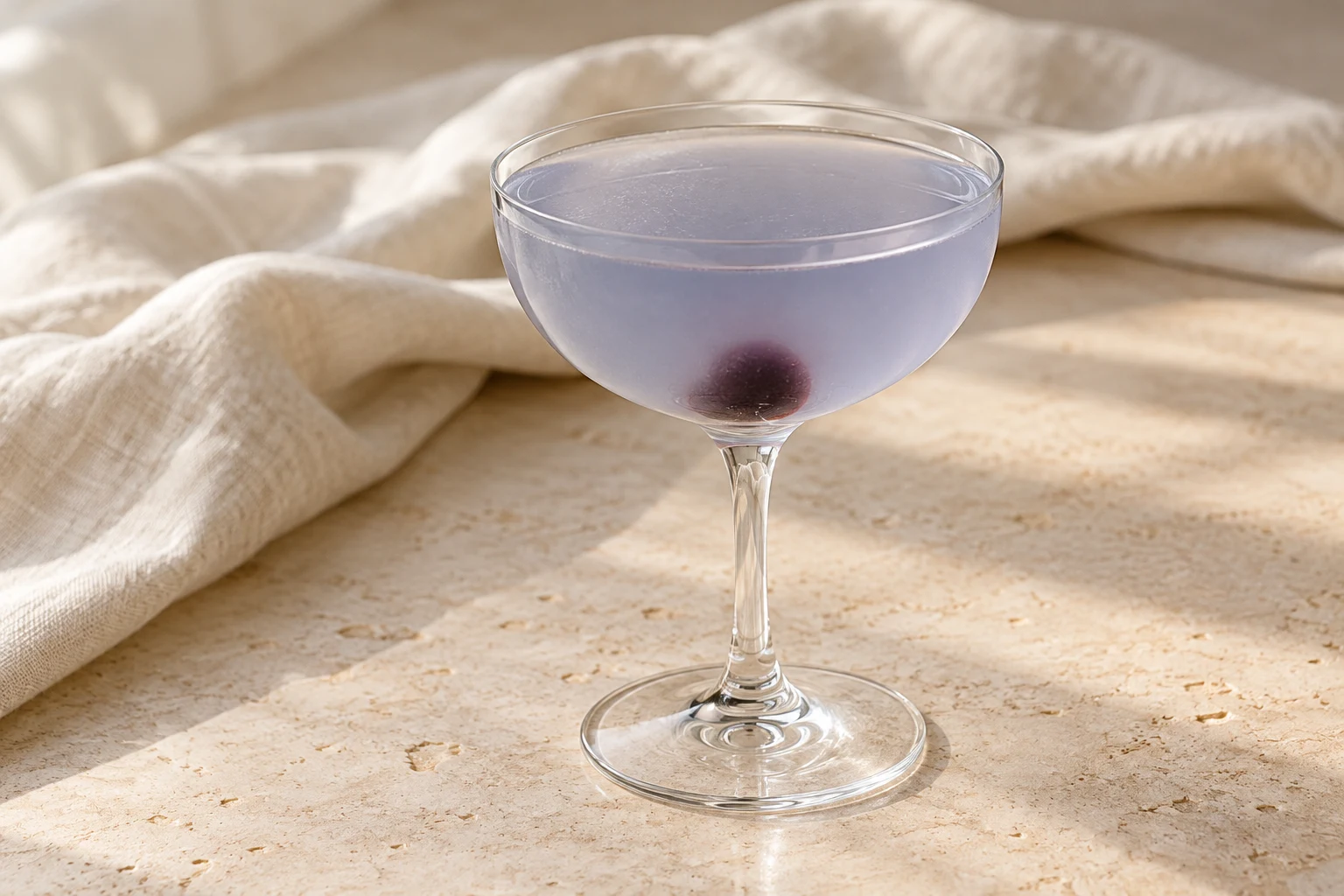 Very pale lavender-blue Aviation in a shallow coupe, without ice, with one small dark cocktail cherry