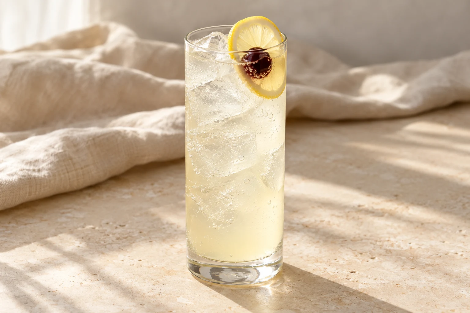 Pale lemon-colored sparkling Tom Collins in a tall ice-filled glass with one lemon wheel and a dark cocktail cherry