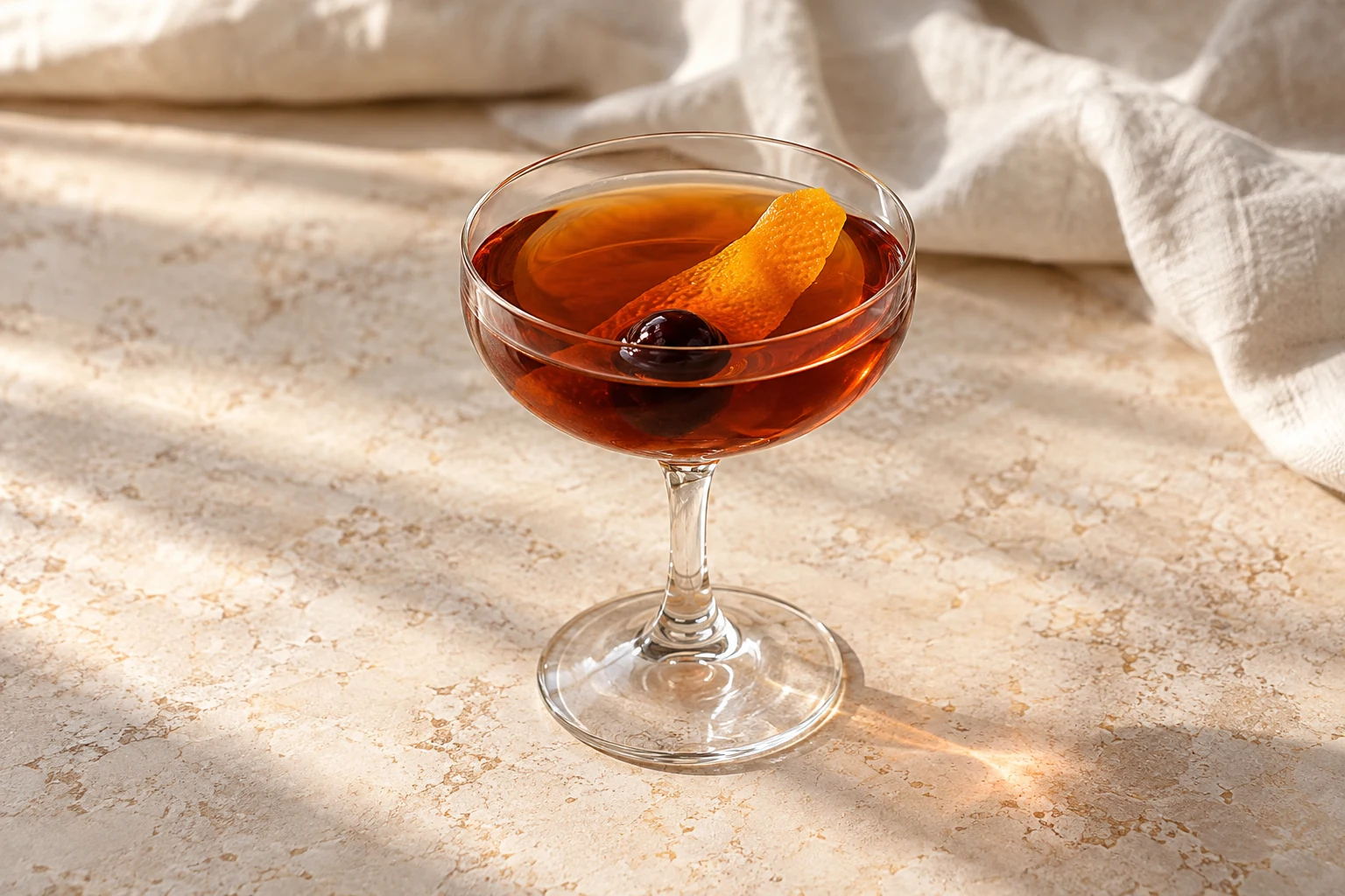 Clear amber Vieux Carré in a small coupe without ice, with an orange peel and one dark preserved cocktail cherry